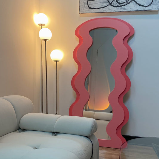 Living room with a pink wavy mirror, white sofa, and decorative items on a table.